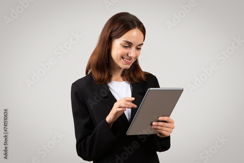 An attentive young businesswoman in a black blazer is focused on a tablet she's holding