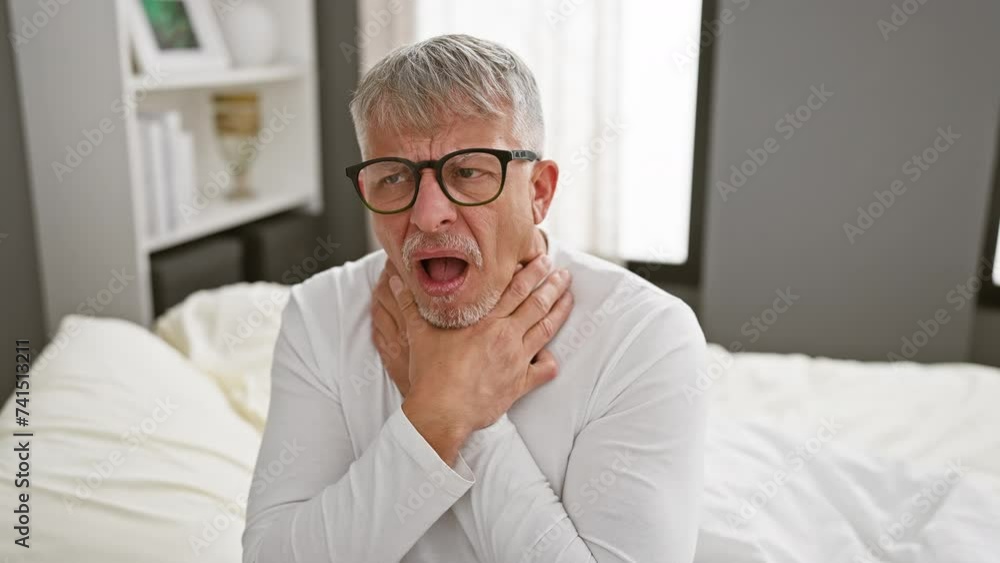 Pain-stricken middle age, grey-haired man writhing in agony, suffocating from a painful strangle in his pyjama, an alarming health problem surfaces in the gloom of his bedroom. Pain-stricken middle age, grey-haired man writhing in agony, suffocating from a painful strangle in his pyjama, an alarming health problem surfaces in the gloom of his bedroom.