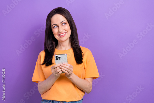 Portrait of smart girl wear oversize t-shirt holding smartphone look at proposition empty space isolated on violet color background