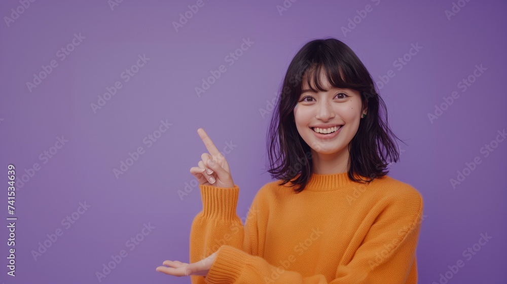 Smiling Japanese woman wearing a bright orange sweater. She is pointing with her right hand, standing against a solid purple background. Smiling Japanese woman wearing a bright orange sweater. She is pointing with her right hand, standing against a solid purple background.