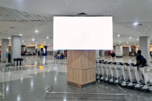 An empty billboard in a crowded airport with a trolley cart in the background. Public space blank LCD screen template