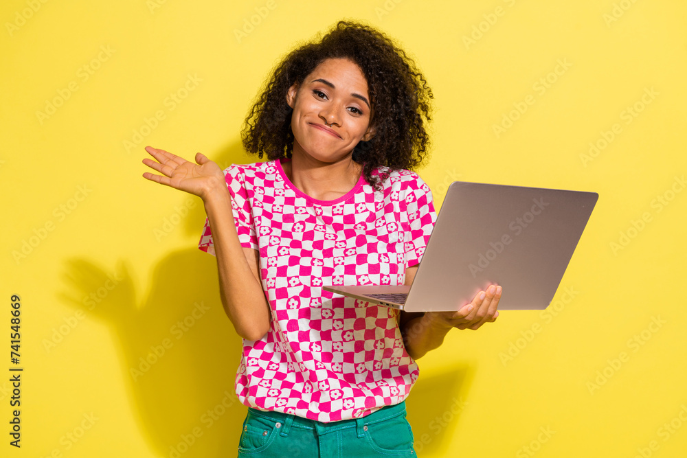 Portrait of attractive clueless person hold wireless netbook raise hand shrug shoulder isolated on yellow color background Portrait of attractive clueless person hold wireless netbook raise hand shrug shoulder isolated on yellow color background