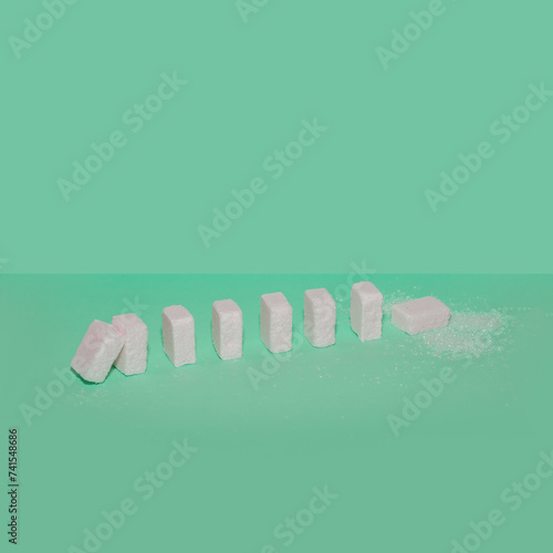 Sugar cubes as domino effect on a green background. Creative food concept. 
