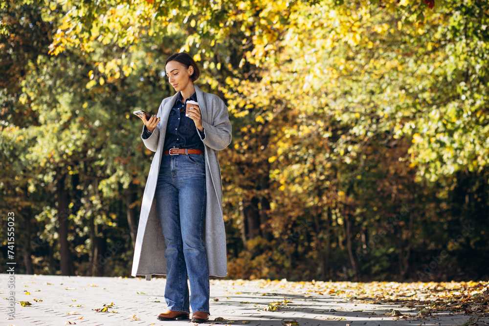 Woman standing in park drinking coffee and using mobile phone Woman standing in park drinking coffee and using mobile phone
