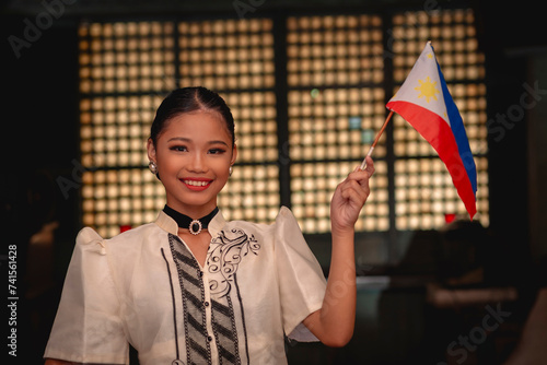 A proud young Filipina lady in a baro’t saya traditional dress, waving the Philippine Flag. Inside an ancestral house. photo