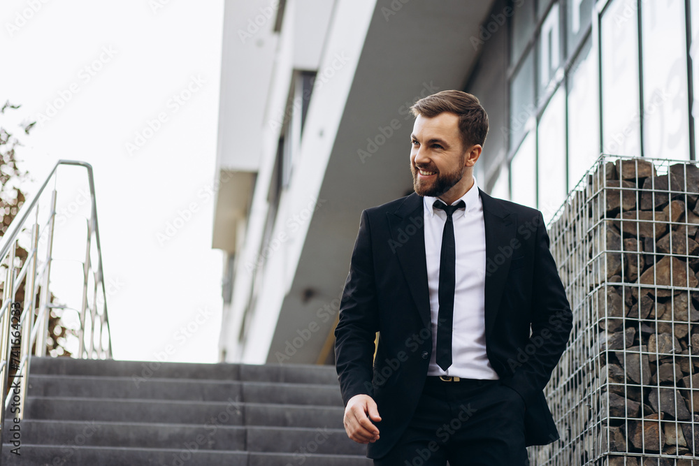 Handsome business man in black suit walking down the stairs by office center Handsome business man in black suit walking down the stairs by office center