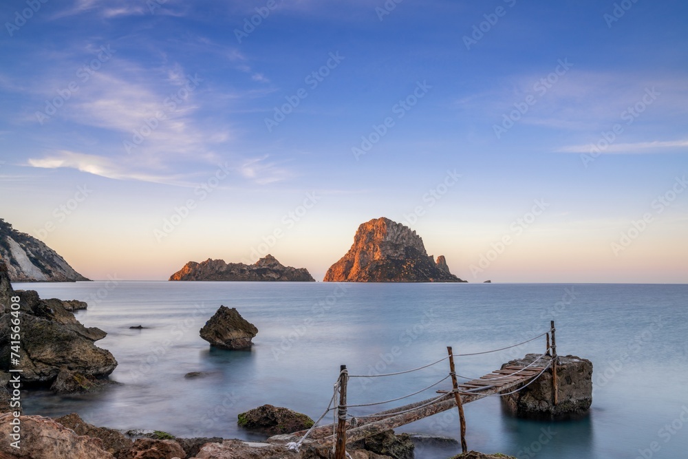 small wooden pier in Cala d'Hort with a view of the Es Vedra rocks in the background at sunrise