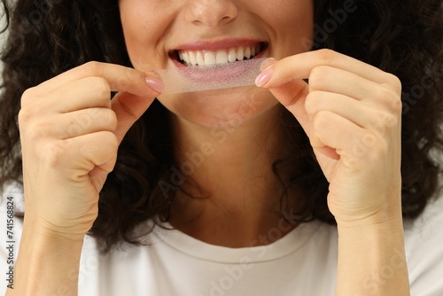 Young woman applying whitening strip on her teeth, closeup