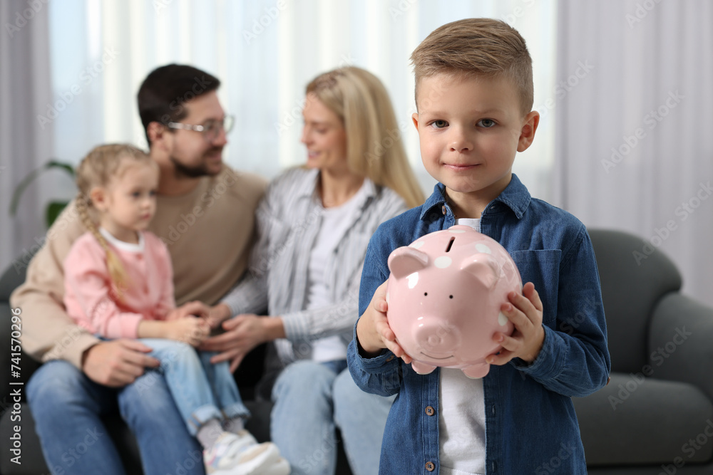 Family budget. Little boy with piggy bank, his parents and sister at home, selective focus