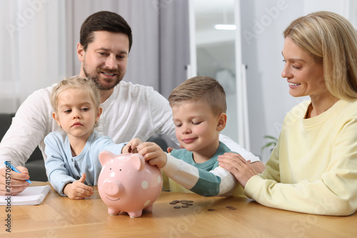 Family budget. Children putting coins into piggy bank while their parents watching at them indoors