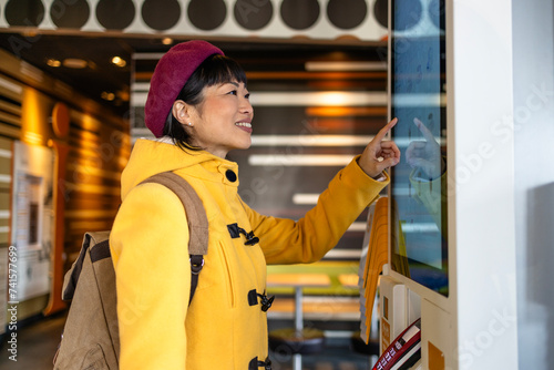 Woman in trendy coat checking menu and ordering meal on self service interactive display inside fast food restaurant. photo