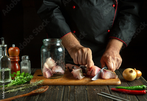 A professional chef cuts carp and prepares herring in a jar with spices. The concept of salting river fish in the kitchen of a public house photo