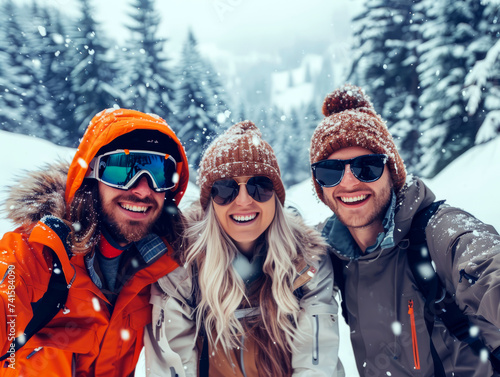 Joyful friends taking a group selfie with the snowy peaks of a mountain range in the background, enjoying a winter day.