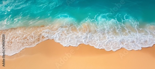 Aerial view of coastal beach with crashing waves, blue water, foam, and sandy shoreline in summer