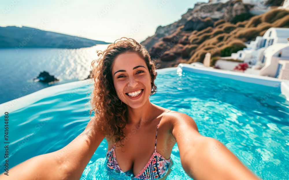 Santorini Selfie Postcard: A Young Native Woman, Radiating Happiness, Takes a Blissful Selfie in a Pool Paradise with Iconic Santorini Houses as the Backdrop.

