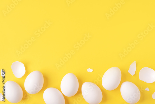 Minimalistic Easter background. White Easter eggs and shells on a bright yellow background. Card with a place for text. Top view.