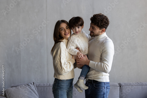 Happy young bearded man cuddling sitting on cozy couch beautiful wife with small son.