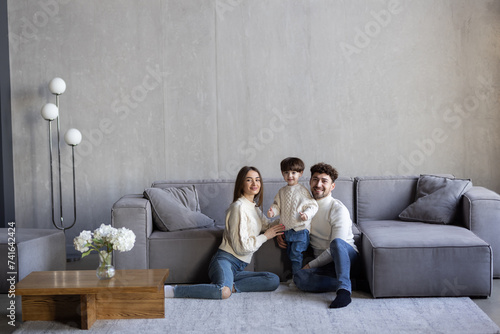 Portrait of excited young parents with cute little son posing in new apartment