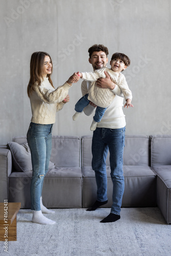 Happy young parents spending leisure time with baby boy on couch at home