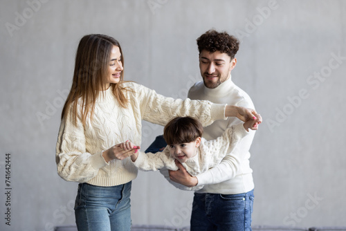 Father and mother smiling and lifting mixed race son near couch in cozy living room