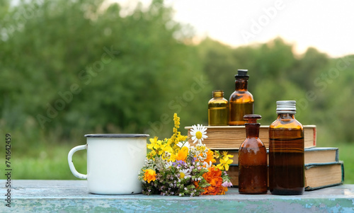 glass bottles with tinctures, books, enamel mug, useful flowers, herbs close up on table in garden, natural background. eco friendly care organic product. Herbal treatment, Spa Cosmetic