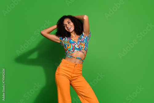Photo of pretty young chevelure hair woman vintage top combinated with orange jeans relaxed touch hair isolated on green color background photo