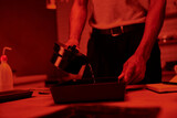 cropped photographer pours developer into a tray for film processing in darkroom with red light