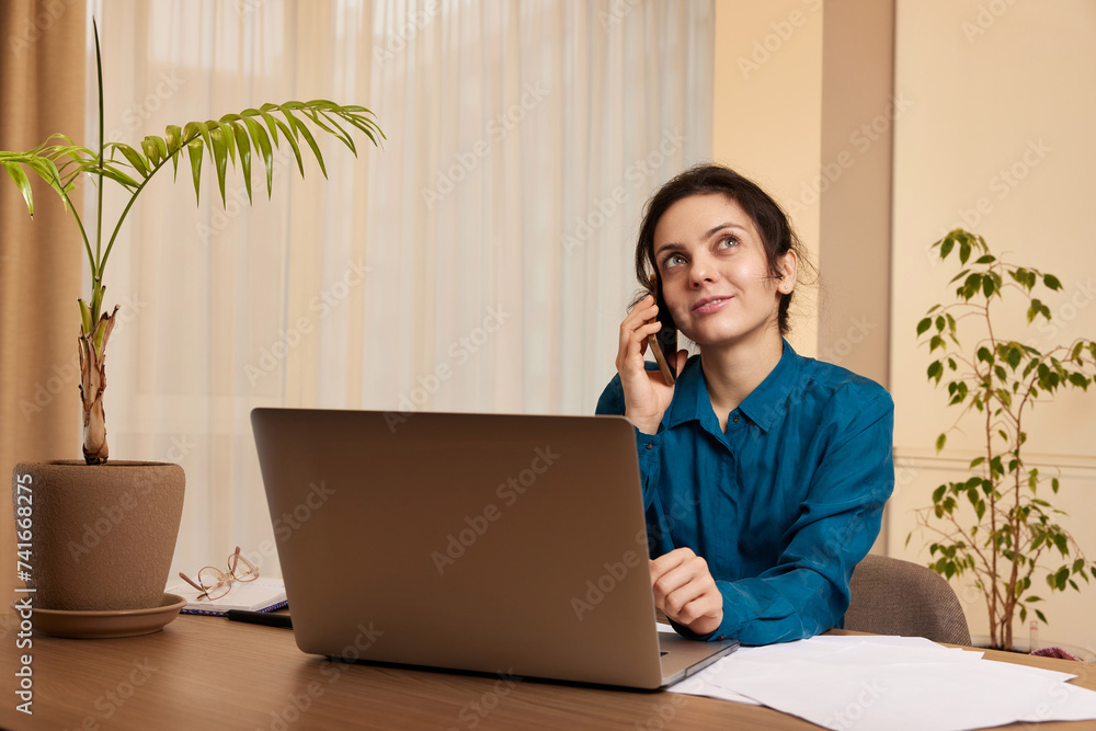beautiful businesswoman working on laptop and communicates with customer by phone at home beautiful businesswoman working on laptop and communicates with customer by phone at home