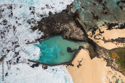 Aerial drone view of large ocean waves breaking over rocks and flooding a tidal pool with children swimming, Boucan Canot, Saint Paul, Reunion. photo