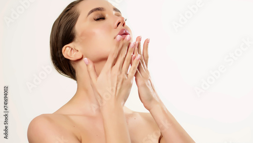Portrait of an attractive dreamy tender girl doing a face and neck massage  isolated on a light background. Self care concept. Advertising of cosmetic products.