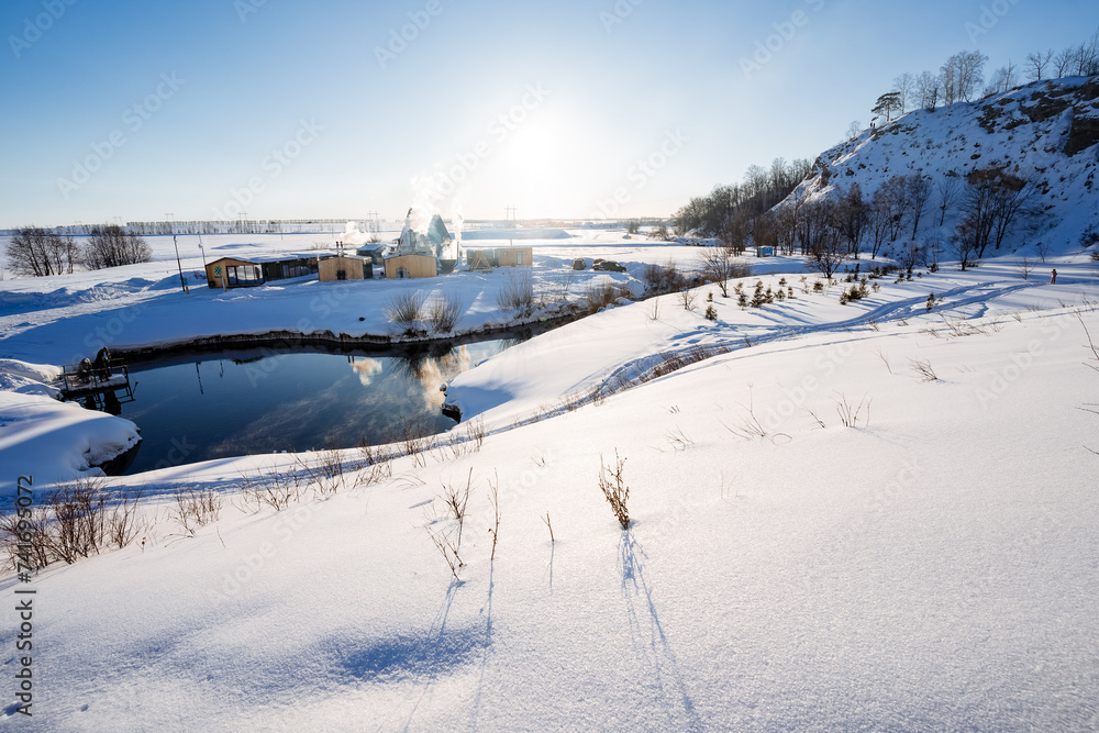 Obraz premium The mountain lake does not freeze in winter, the sun sets below the horizon, deep snowdrifts, a beautiful landscape. Frosty weather.