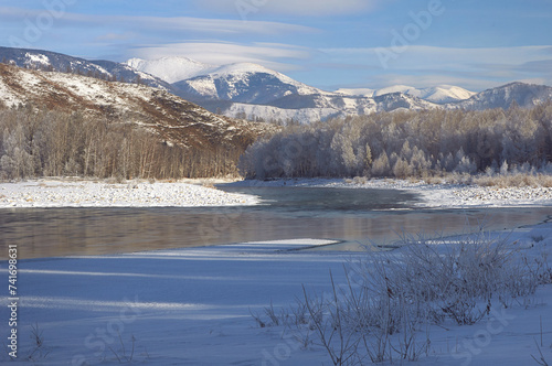 Snowcovered mountain landscape with a frozen river and cloudy sky.