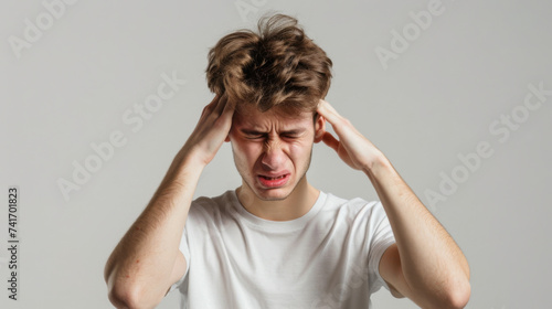man in visible distress, with his eyes tightly shut and hands pressed against his temples, suggesting he is experiencing a severe headache or migraine.