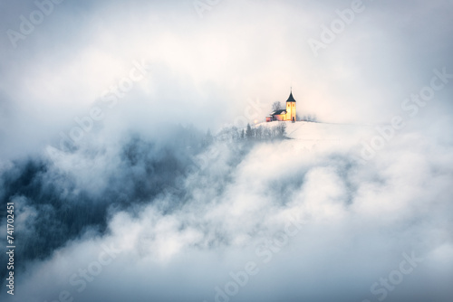 The Church of St Primoz and Felicijan on slopes of Velika Planina through the clouds, Jamnik, Kranj, Slovenia photo