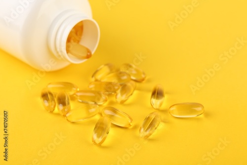 Vitamin capsules and medical bottle on yellow background, closeup