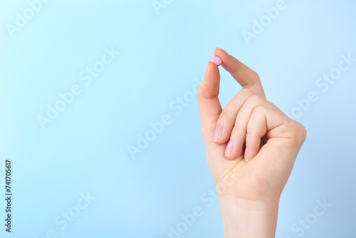 Woman holding vitamin pill on light blue background, closeup. Space for text