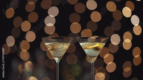 dos copas con martini, aparecen dos manos para tomarlas y brindar. La mano pertenece a una mujer y a un hombre. Fondo de luces bokeh desenfocadas. photo