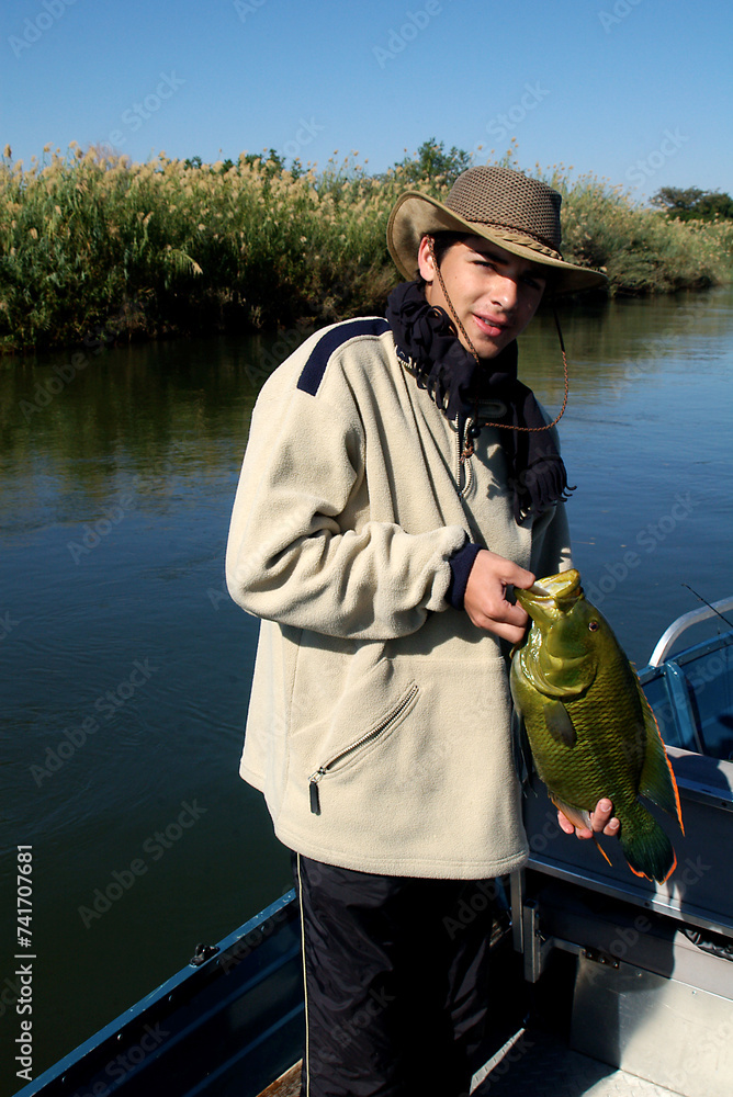 Portrait of a proud teenage boy holding a catch of fish, Okavango River, Botswana Portrait of a proud teenage boy holding a catch of fish, Okavango River, Botswana