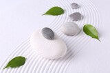 Zen garden stones and green leaves on white sand with pattern