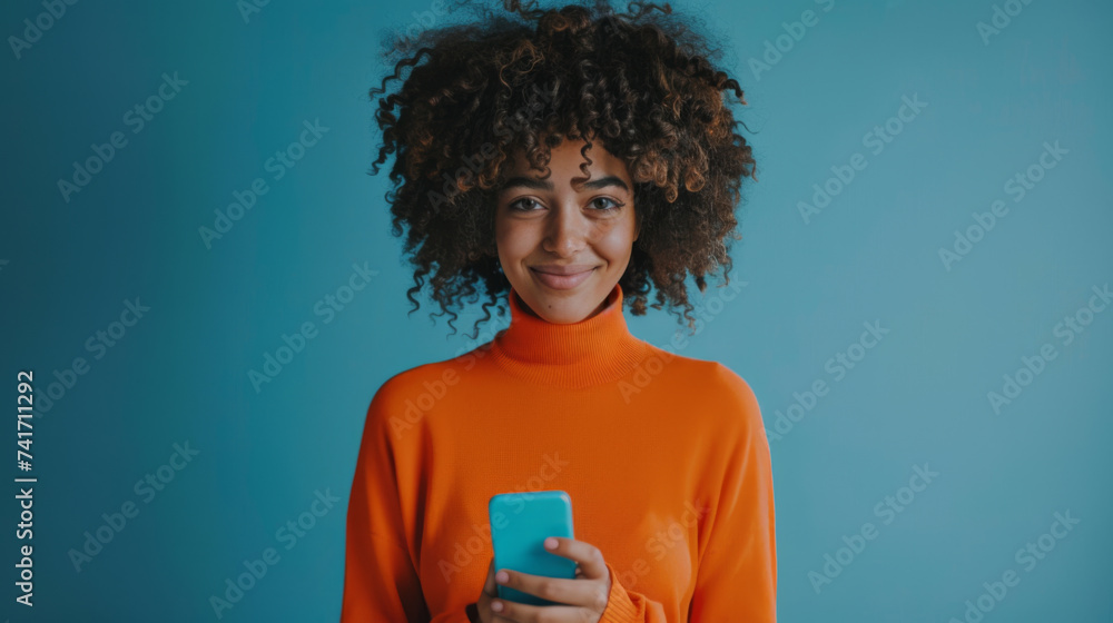 A person in a bright orange sweater is engaged with a smartphone, standing against a solid blue background. A person in a bright orange sweater is engaged with a smartphone, standing against a solid blue background.