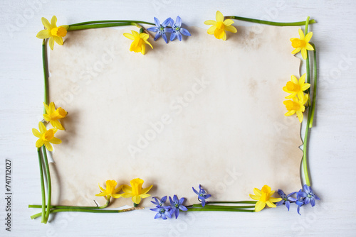 Spring yellow daffodils, blue scilla flowers on white wooden background and paper for greeting text photo