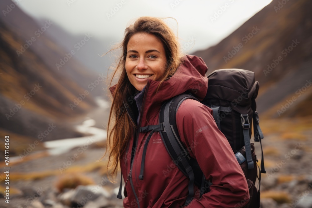 Young woman hiker standing on the trail with backpack and looking at camera