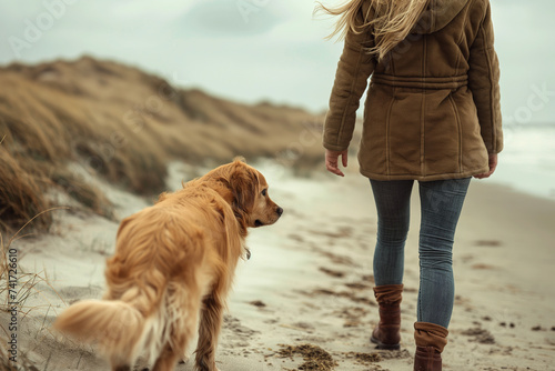 A young woman walks with her golden retriever dog along the seashore #741726610