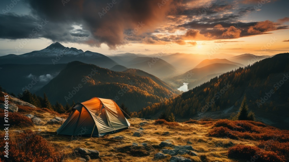Camping in the mountains at sunset. The tent stands on a grassy hilltop against the backdrop of a beautiful mountain landscape.