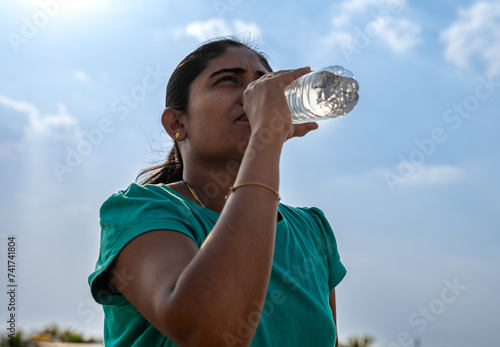 Young woman drinking water from a bottle after jogging in the park