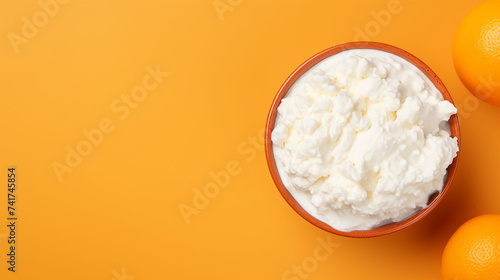 Cottage cheese in a bowl with oranges on orange background. Top view photo