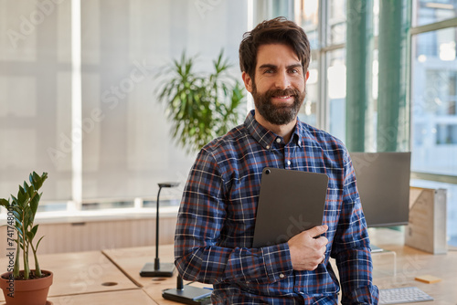 Fotografía Smiling businessman leaning on his desk holding a digital tablet
