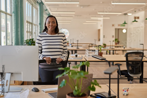 Confident young African businesswoman standing by her desk in an office