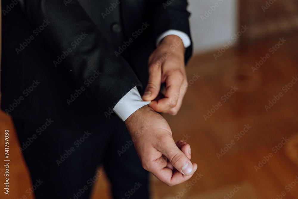 Obraz premium young smiling man buttoning up his jacket in the morning before the wedding. close-up of a man in a business suit. Businessman puts on a suit. A man fastens the buttons on his jacket.