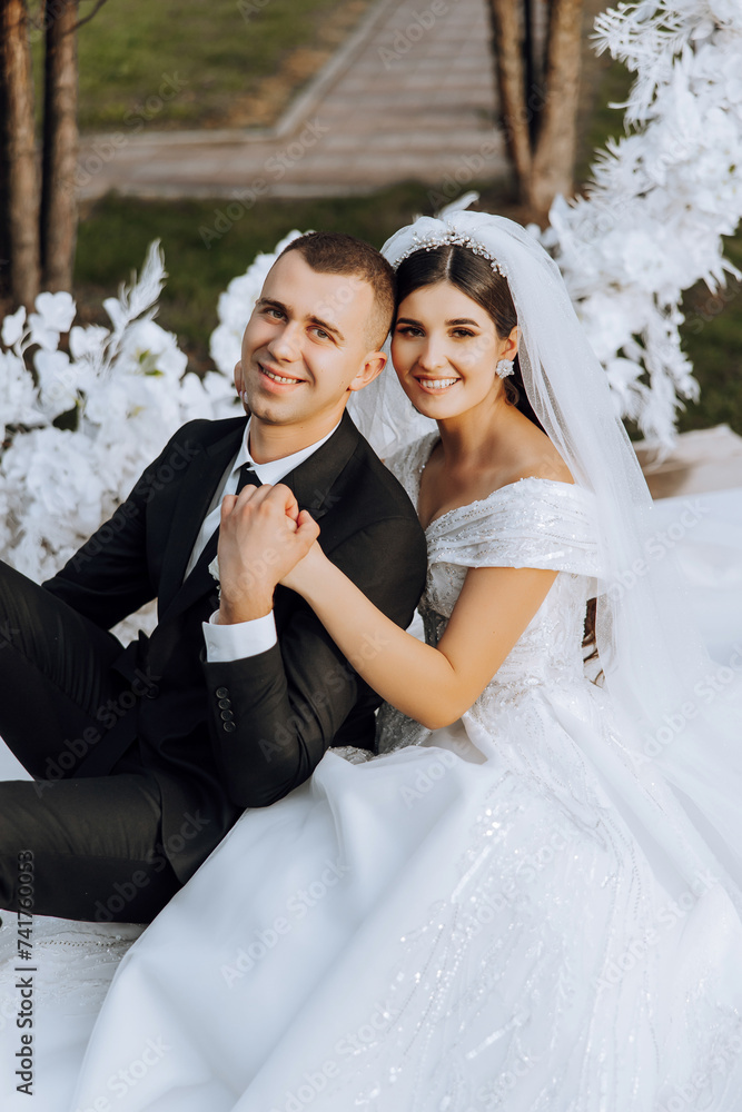 Naklejka premium lovely and stylish newlyweds are hugging and smiling against the background of autumn nature in a beautiful garden. An incredibly beautiful young bride leaned against the shoulder of her beloved groom